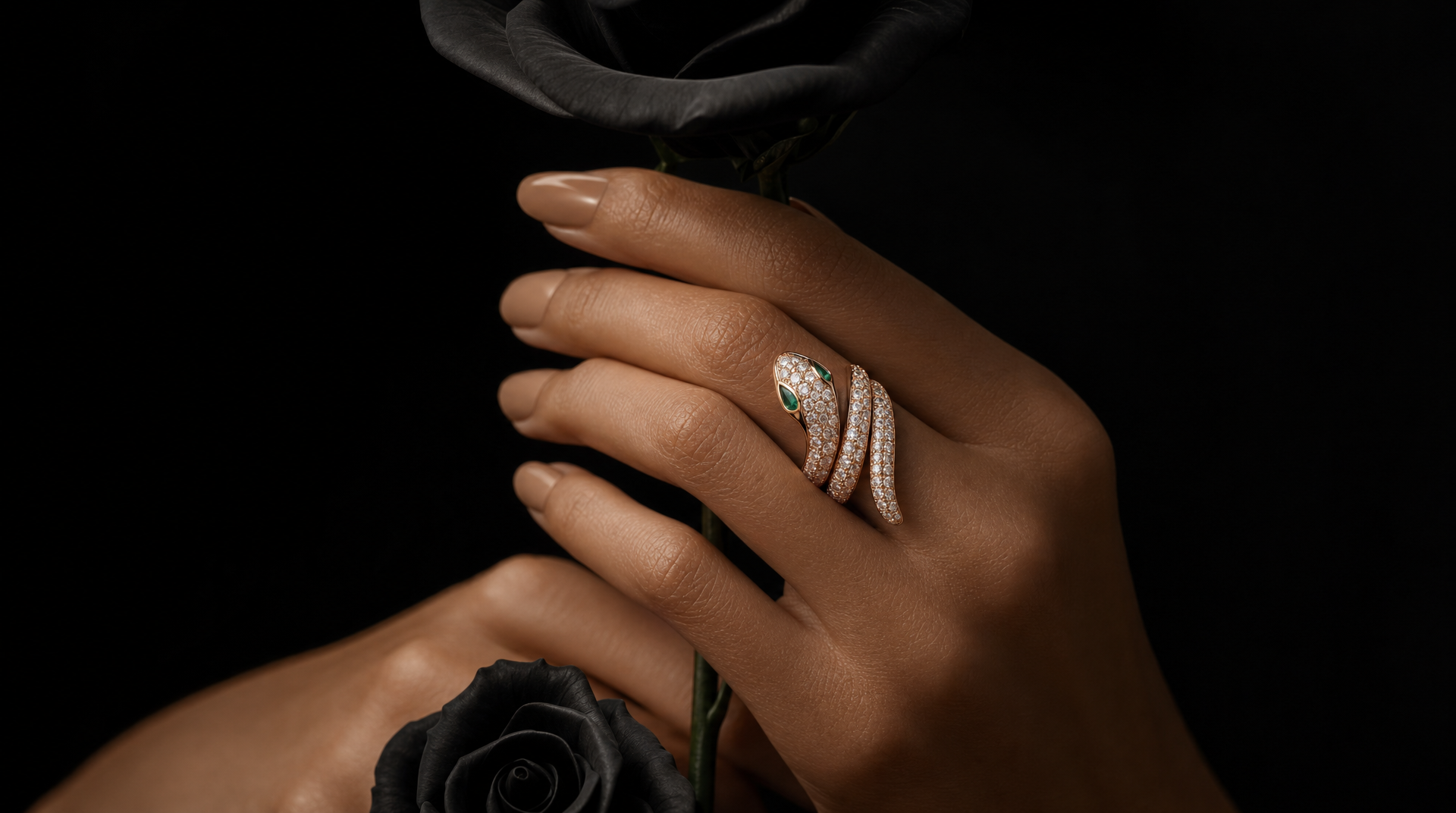 A wide 16:9 cinematic jewelry fashion editorial photograph of a female model's hands center frame, holding a single long stemmed black rose. She wears the Bulgari Serpenti Viper ring in 18k rose gold with full pavé diamonds coiling around her index finger, the snake head set with two emerald eyes catching the light at the highest point of the coil. Dramatic single-source side lighting from the left creates deep shadow on the right side of both hands, making the diamonds on the ring blaze against the darkness. The black rose petals frame the ring from above and below. Background: seamless deep black. Shot on an 85mm lens at f/2.8. Color grade: rose gold warmth, absolute black background, emerald green eye accents, the diamond pavé blazing white against the darkness. Mood: dark luxury, dramatic, editorial high jewelry campaign.